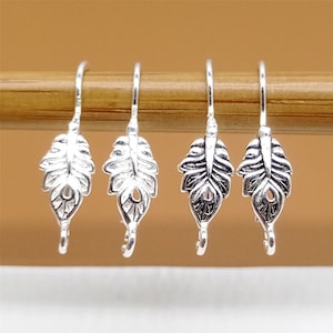 May include: Four silver leaf-shaped earring hooks. The hooks are delicate and have a detailed design.