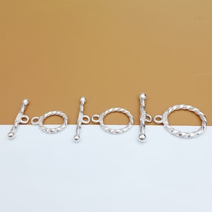 May include: Four silver toggle clasps with a twisted rope design. Each clasp has a round ring on one end and a bar with a round end on the other.