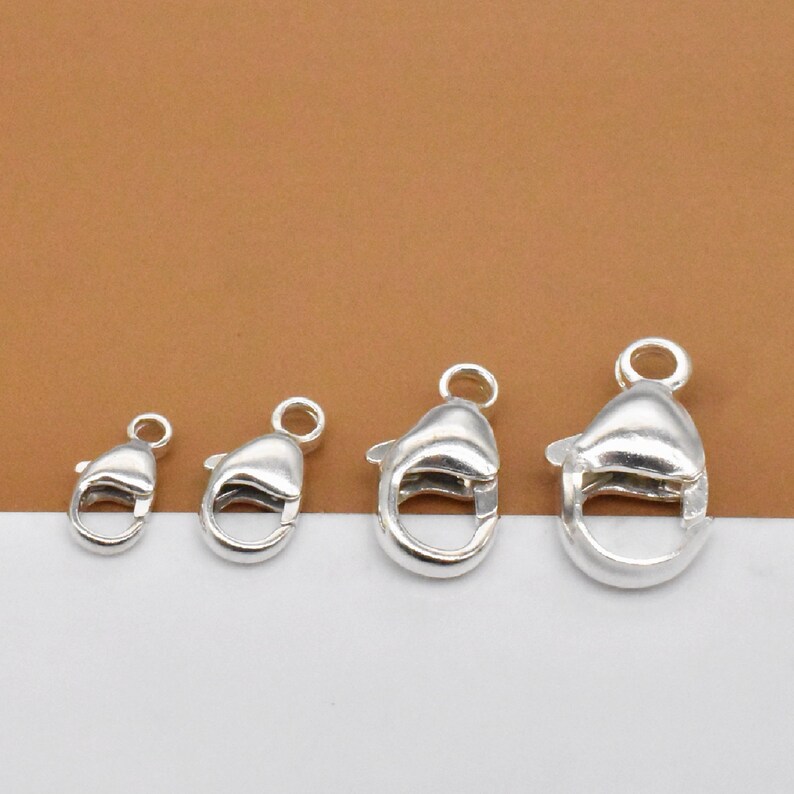 K&ouml;nnte beinhalten: Vier silberne Karabinerverschl&uuml;sse in verschiedenen Gr&ouml;&szlig;en. Die Verschl&uuml;sse sind ein beliebtes Schmuckzubeh&ouml;r f&uuml;r Halsketten, Armb&auml;nder und andere Schmuckprojekte.