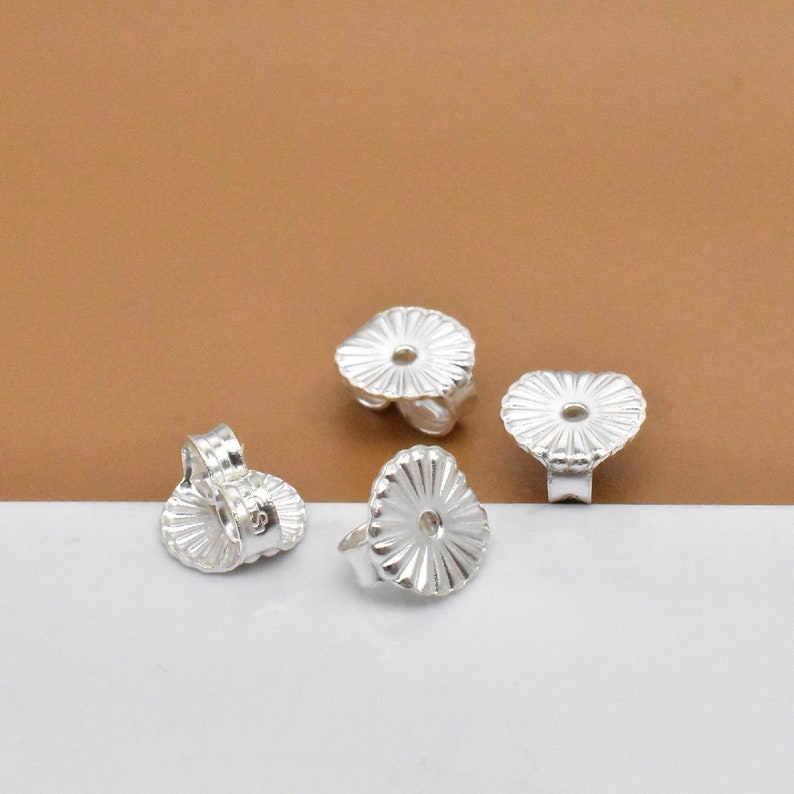 May include: Four silver earring backs with a ridged design. The backs are designed to fit over the post of an earring.