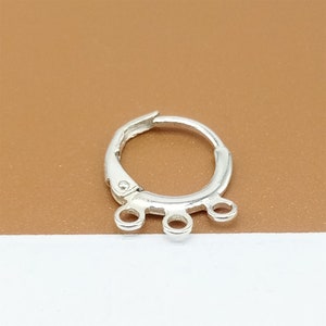 May include: Silver hoop earring with three jump rings hanging from the bottom.