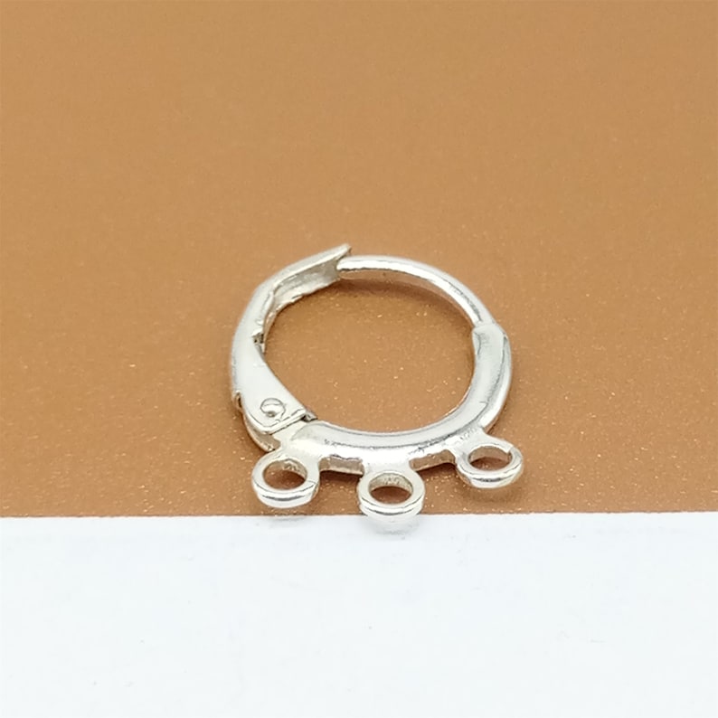 May include: Silver hoop earring with three jump rings hanging from the bottom.