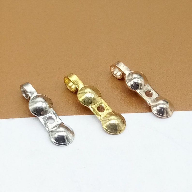 May include: Three metal jewelry findings with a loop at the top and two round balls. The findings are silver, gold, and rose gold.