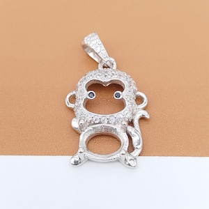 May include: A silver monkey pendant with a bail at the top. The monkey's face has two black eyes and is surrounded by small, clear stones. The pendant has a large, open space where a stone could be set. The monkey's tail curls around its body.