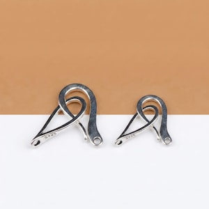 May include: Two silver-coloured, abstract-shaped jewellery clasps. Each clasp has a looped top and a pointed bottom with a small hole. The clasps are marked with "S925". One clasp is slightly smaller than the other.
