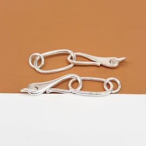 May include: Two silver-toned lobster claw clasps with oval rings. The clasps are open and ready to be attached to a necklace or bracelet.