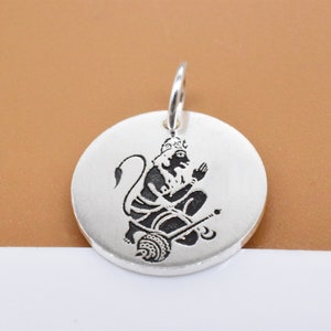 May include: Silver pendant featuring a black and white image of the Hindu deity Hanuman in a seated pose.