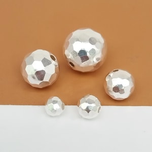 May include: Five silver hammered metal beads of varying sizes. The beads are round and have a textured surface.