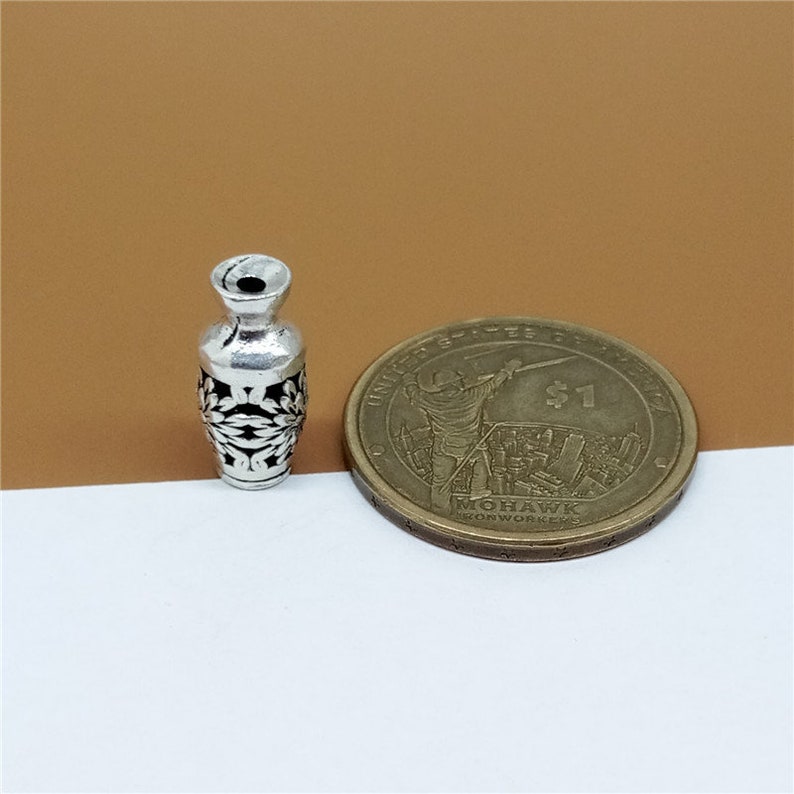 K&ouml;nnte beinhalten: Silberner Vasen-Anh&auml;nger mit einem filigranen Design. Die Vase ist etwa so gro&szlig; wie eine 1-Euro-M&uuml;nze.