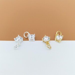 以下が含まれることがあります： 銀色の金属製チャーム2個と金色の金属製チャーム2個。それぞれ、4本爪の台座にセットされた透明なラウンドカットのキュービックジルコニアが1粒あしらわれており、上部には小さな丸カンが付いています。