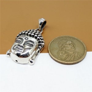 May include: Silver pendant featuring a detailed Buddha head with closed eyes. The pendant is shown next to a US dollar coin for size comparison.