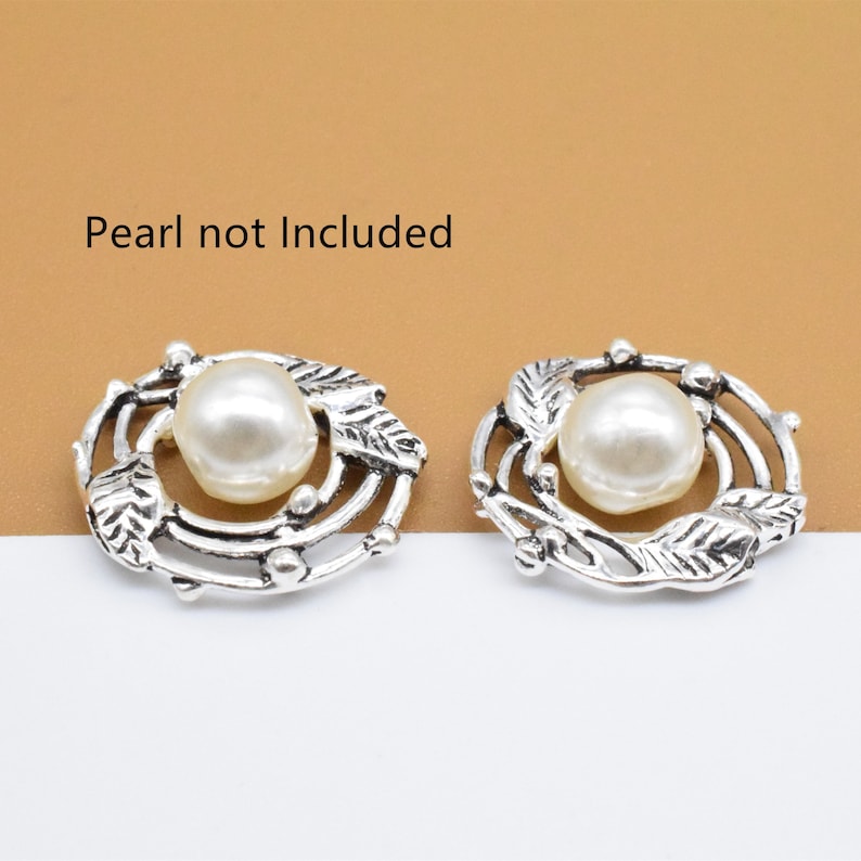 May include: Two silver-toned metal embellishments with a circular design featuring a swirl of leaves and a small pearl in the center.  Pearl not included.