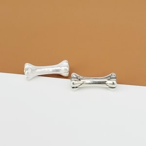 May include: Two silver bone-shaped charms, one with a smooth finish and the other with a textured finish.