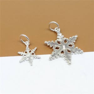 May include: Two silver snowflake charms, one larger than the other, with a loop at the top for attaching to a necklace or bracelet.