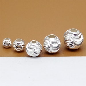 May include: Four silver beads with a wavy design. The beads are different sizes and are arranged in order from smallest to largest.