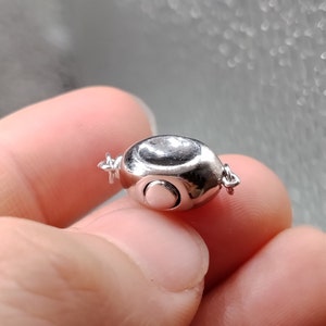 May include: Silver magnetic clasp for a necklace or bracelet. The clasp is round and has a smooth, polished finish. It features a small, round magnet on one side and a matching metal piece on the other side.