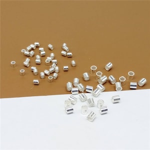 May include: A large quantity of silver-colored metal jump rings. The jump rings are small and cylindrical in shape. They are scattered on a brown surface and a white surface.