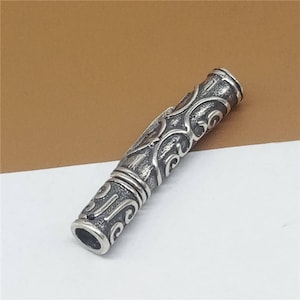 Puede incluir: Pendiente de plata con un diseño intrincado y ornamentado. El pendiente es cilíndrico y tiene un acabado liso y pulido.