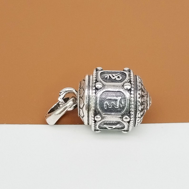 Puede incluir: Encanto de plata en forma de rueda de oraci&oacute;n con detalles intrincados y s&iacute;mbolos grabados. El encanto tiene un bucle para sujetarlo a un collar o pulsera.
