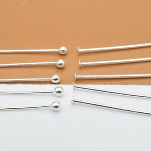 May include: A set of silver head pins with round heads. The pins are arranged in two rows, with the heads facing up. There are six pins in each row.