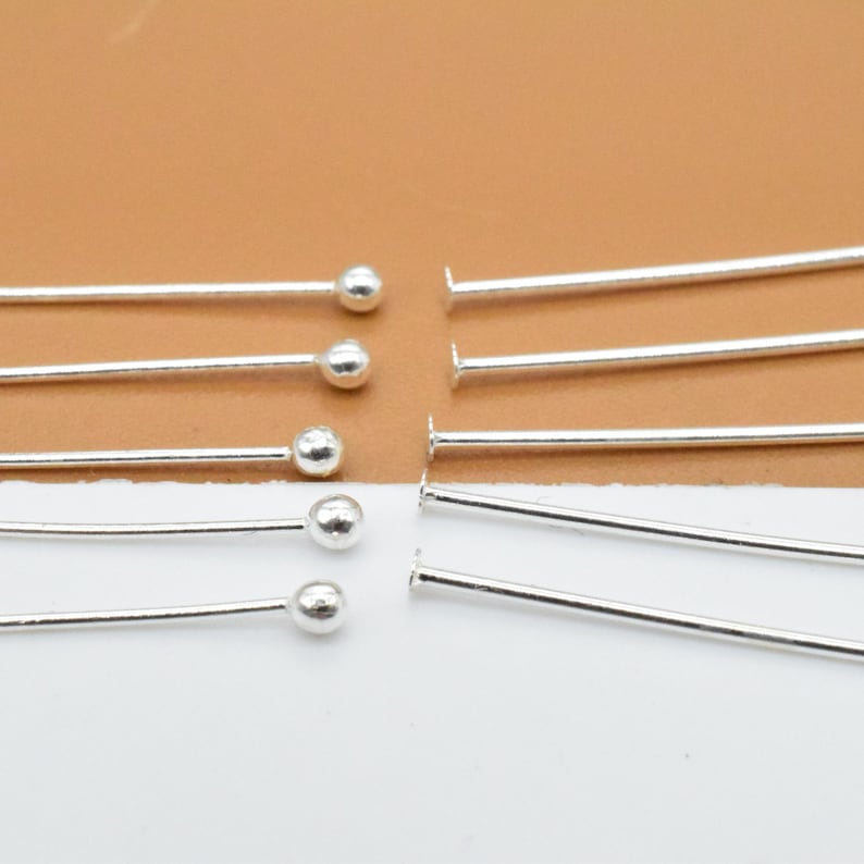 May include: A set of silver head pins with round heads. The pins are arranged in two rows, with the heads facing up. There are six pins in each row.