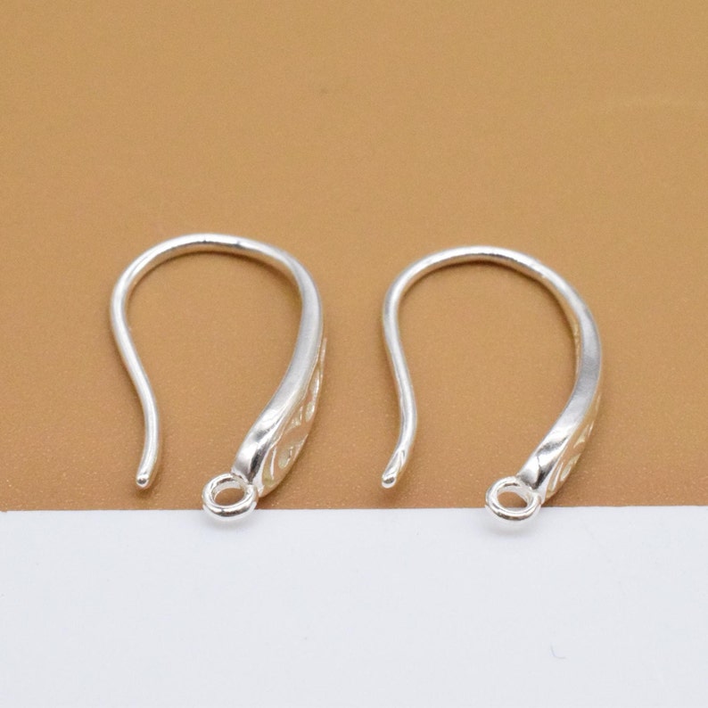 May include: Two silver earring hooks with a decorative design. The hooks are made of metal and have a smooth finish.