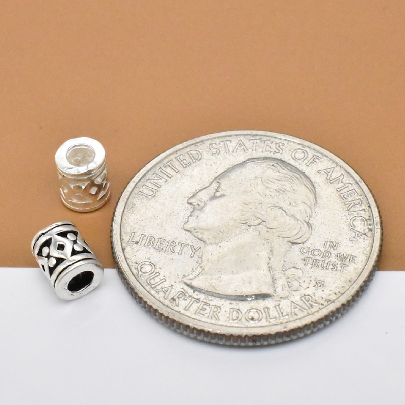May include: Two silver metal beads with a geometric design, next to a US quarter for size comparison.