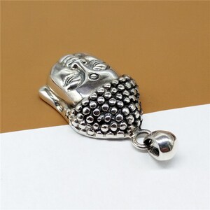 May include: Silver pendant featuring a detailed Buddha head with a textured design. The pendant has a loop for attaching to a chain.