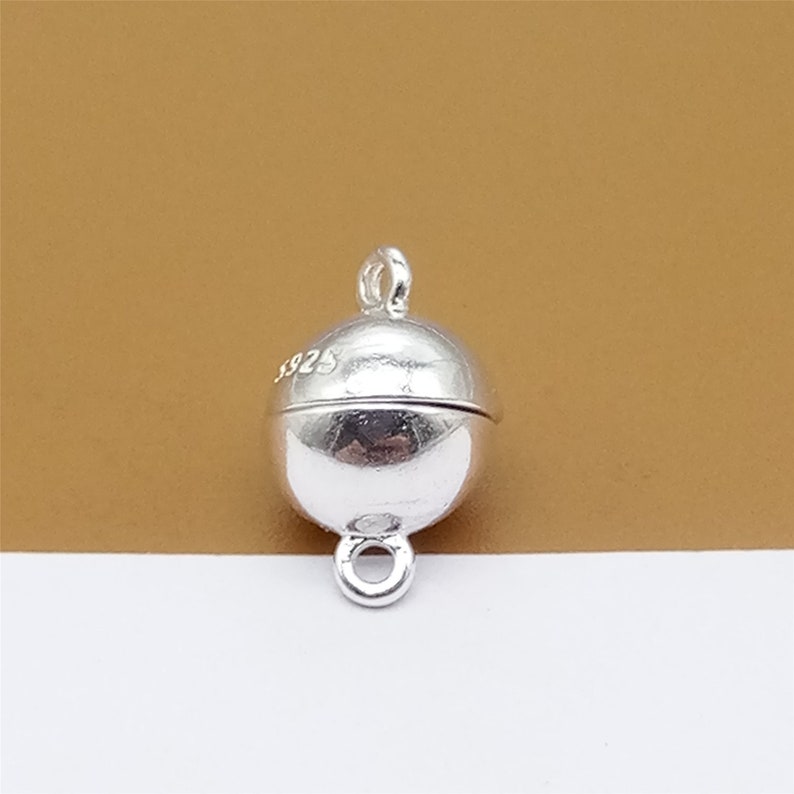 May include: Silver magnetic clasp for jewelry making. The clasp is round and has a smooth, polished finish. The clasp is marked with the number "925" on the side.