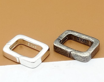 Puede incluir: Dos cierres cuadrados de plata con una abertura con bisagra. El cierre de la izquierda es de plata pulida y el cierre de la derecha es de plata oxidada más oscura. Ambos cierres tienen la inscripción "S925" en el lateral.