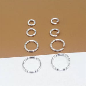 May include: A set of eight silver jump rings in various sizes. The jump rings are arranged in two rows of four.