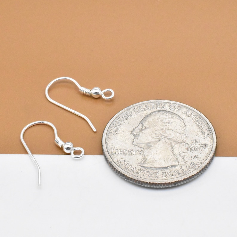 May include: Two silver earring hooks with a small ball at the end of each hook. The hooks are shown next to a US quarter for size comparison.