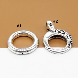 Könnte beinhalten: Zwei silberne 925er Sterlingsilber-Verschlüsse. Der erste Verschluss ist ein einfacher runder Ring. Der zweite Verschluss ist ein verzierterer Ring mit einem dekorativen Design.