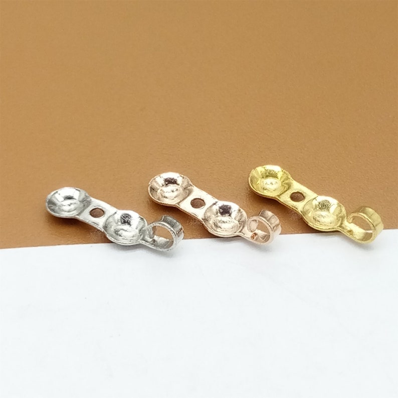 May include: Three metal jump rings with a loop on one end and two round holes on the other. The jump rings are silver, gold, and rose gold.