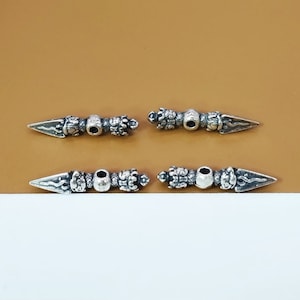 May include: Four silver-toned metal charms shaped like a stylised dagger with intricate details. The charms have a hole in the centre for attaching to a bracelet or necklace.