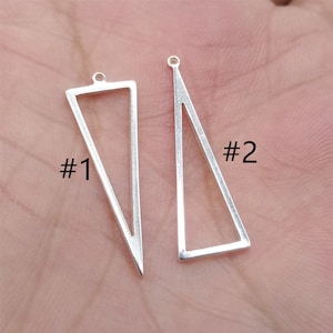 May include: Two silver triangle pendant charms, one with a solid outline and the other with an open outline. The charms are labelled #1 and #2.