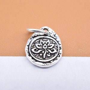 Può includere: Ciondolo in argento con un design dettagliato di fiore di loto. Il ciondolo ha una superficie testurizzata e un anello per attaccarlo a un braccialetto o una collana.