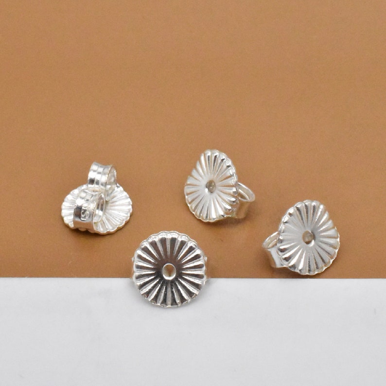 May include: Four silver earring backs with a ridged, circular design. The backs have a small hole in the center.