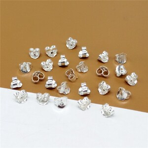 May include: A collection of silver earring backs, also known as earring stoppers, for securing earrings. The backs are designed with a small loop for the earring post and a curved back to fit comfortably against the earlobe.