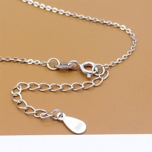 Op de afbeelding: Close-up van een zilveren ketting met een karabijn sluiting en een klein label met de tekst "925".