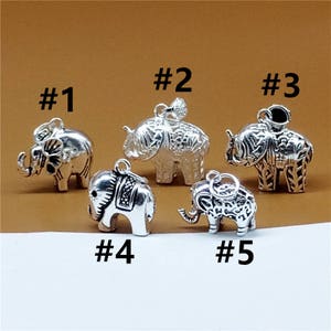 Puede incluir: Cinco encantos de elefante de plata con detalles intrincados. Cada encanto está numerado del 1 al 5. Los encantos están sobre un fondo marrón.