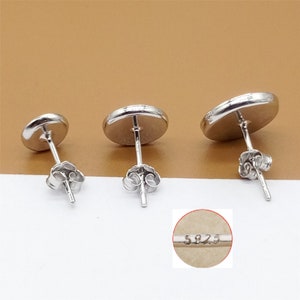 May include: Three silver stud earrings with round, flat tops. The earrings have a post and butterfly backing. The back of one earring has the marking "S925".