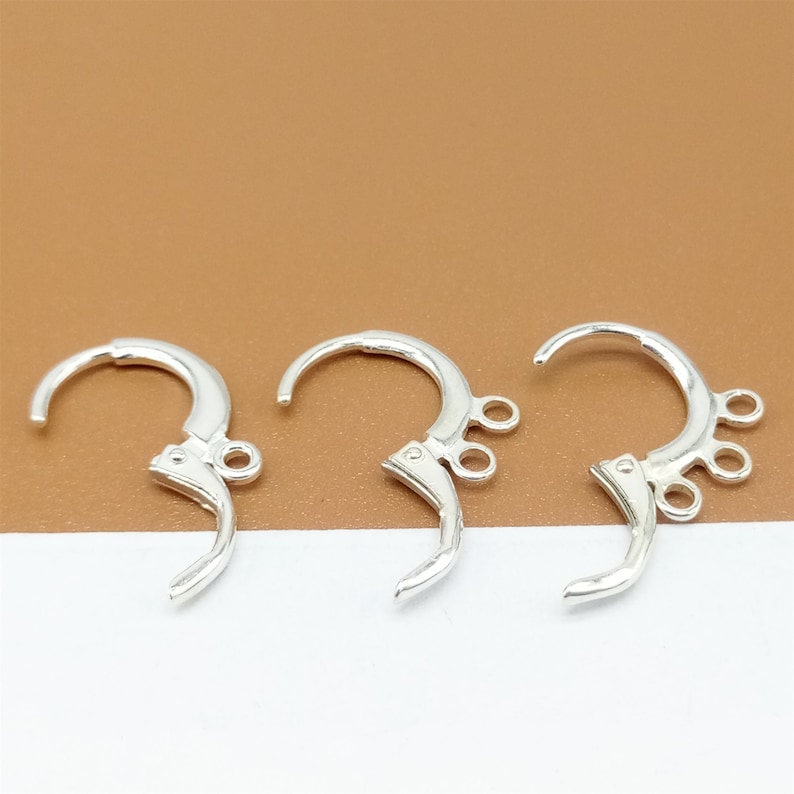 May include: Three silver earring hooks with three loops on each hook. The hooks are designed to be used for attaching earrings to a necklace or bracelet.