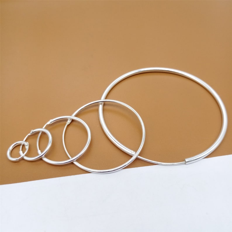 May include: Set of five silver hoop earrings of varying sizes. The hoops are all smooth and have a polished finish.