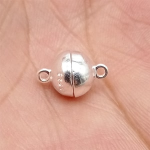 May include: Silver magnetic clasp for jewelry making. The clasp is round and has a smooth, polished finish. The clasp is marked with the number "925" indicating it is made of sterling silver.