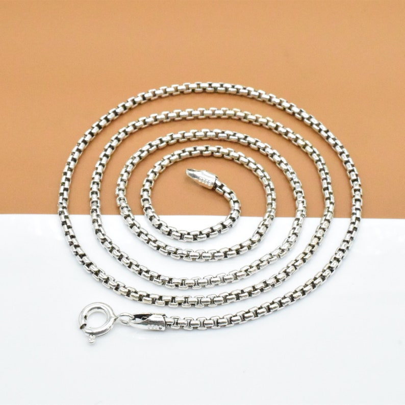 May include: A silver chain necklace with a lobster clasp. The chain is made of small, linked squares.