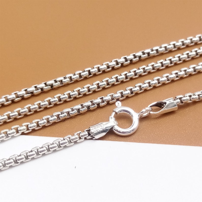 May include: A silver chain necklace with a box chain design and a lobster clasp closure.