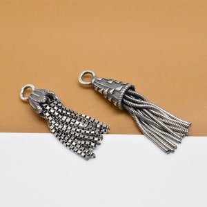 May include: Two silver tassel charms with a detailed design. The tassels are made of small silver chains.