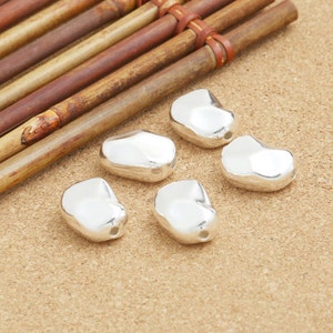 May include: Six silver-colored, smooth, bean-shaped beads with a hole in the center.