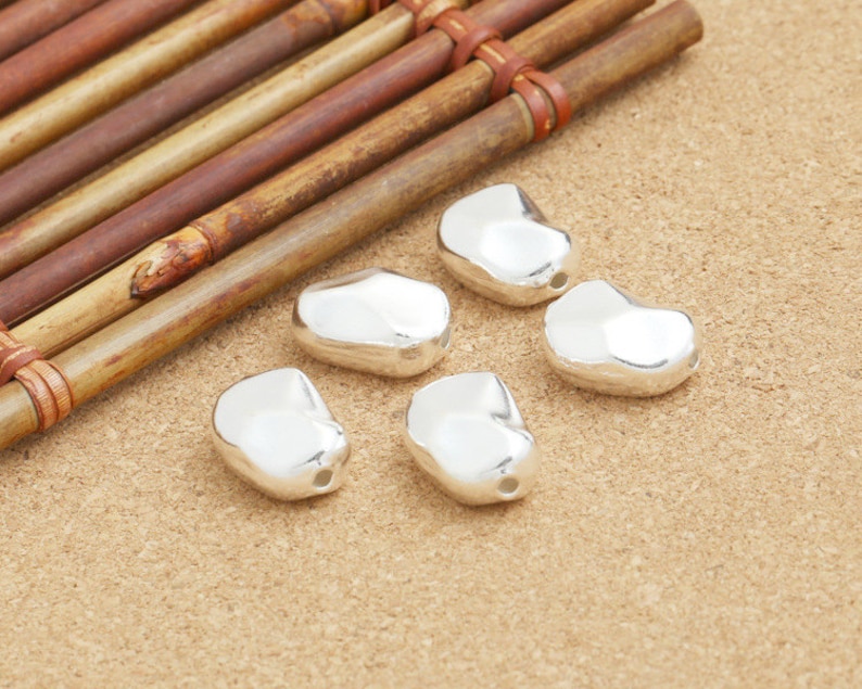 May include: Six silver-colored, smooth, bean-shaped beads with a hole in the center.
